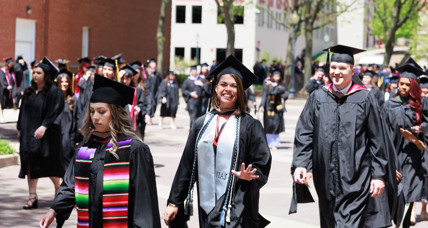 graduate students walking with diplomas at commencement
